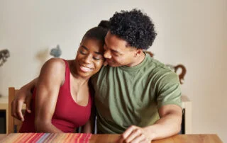A black woman and man hugging while at the dinner table.